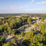 Aerial view of a suburban neighborhood surrounded by dense trees and a distant hill on the horizon under a clear sky